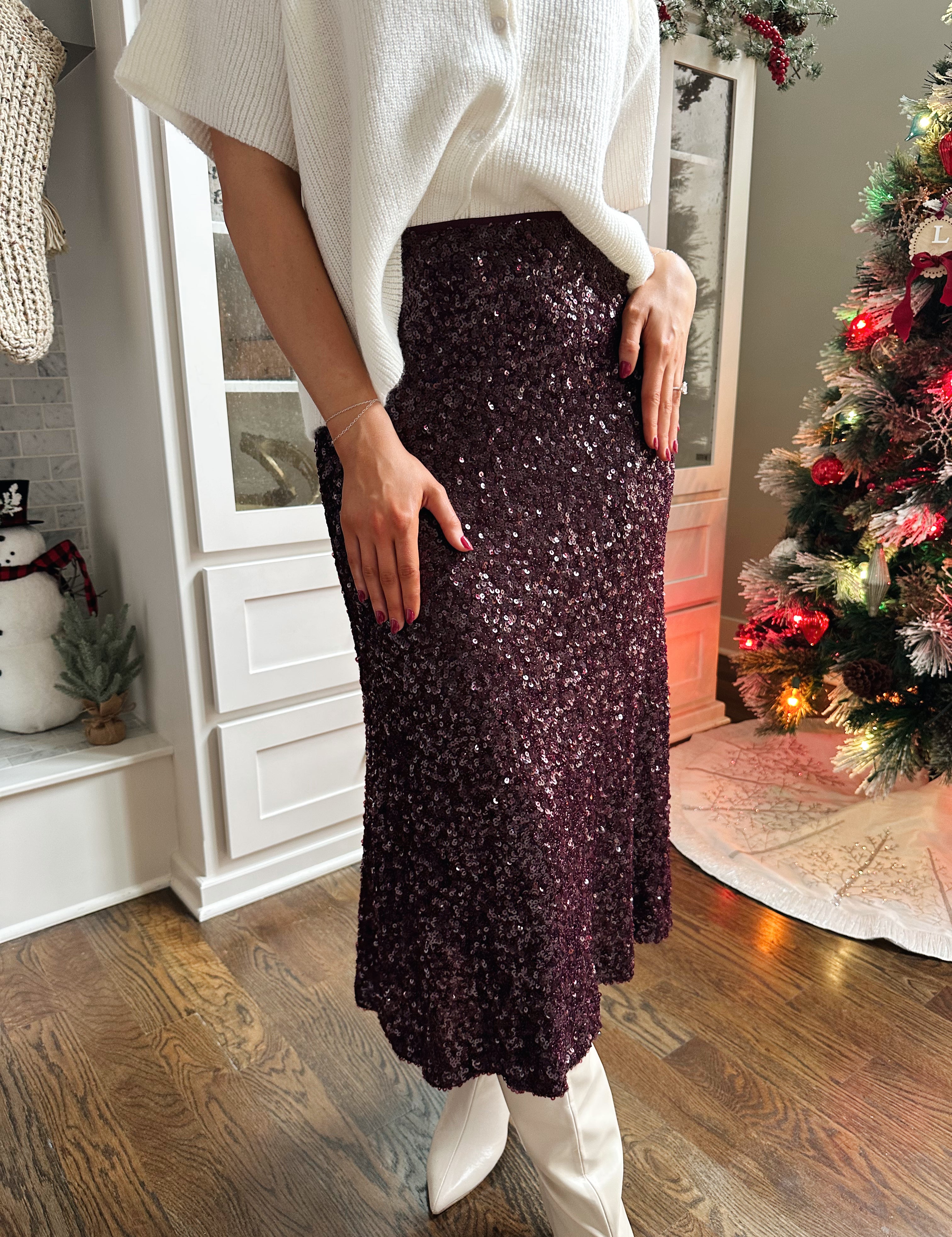 Woman wearing burgundy sequin midi skirt with knit button up sweater top.