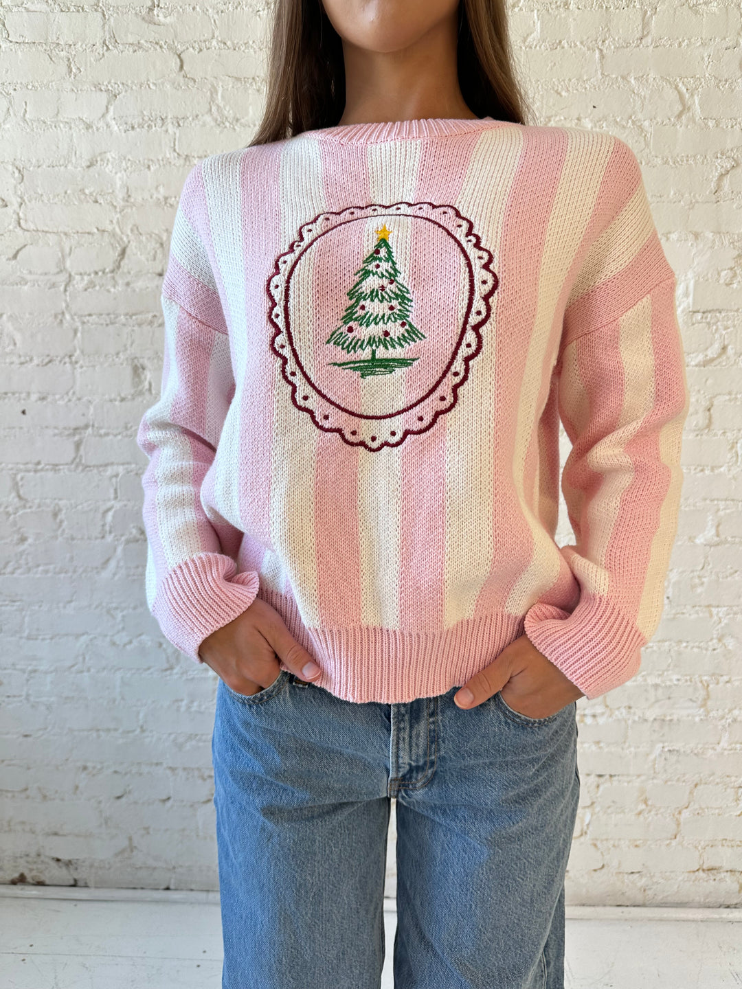 Woman wearing pink and white knit striped sweater with embroidered Christmas tree. 