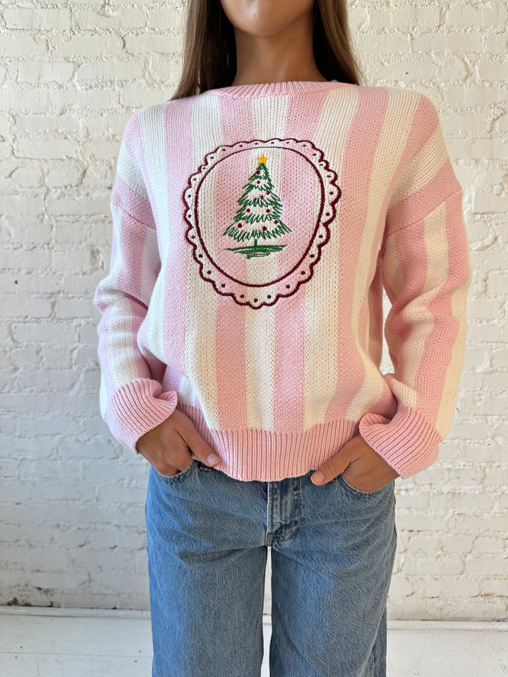 Woman wearing pink and white knit striped sweater with embroidered Christmas tree. 