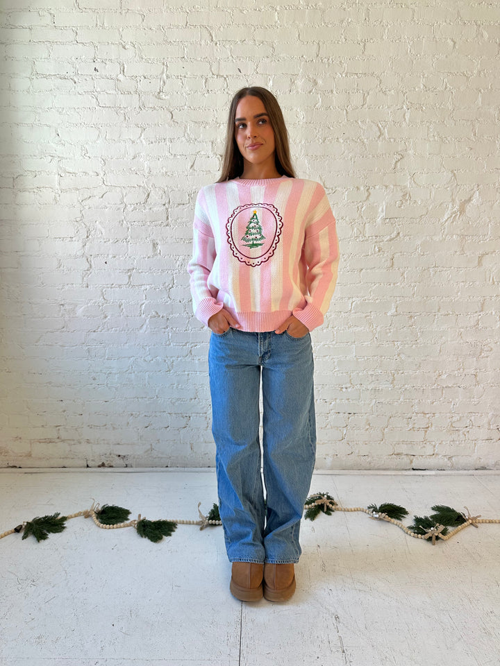 Woman wearing pink and white knit striped sweater with embroidered Christmas tree. 