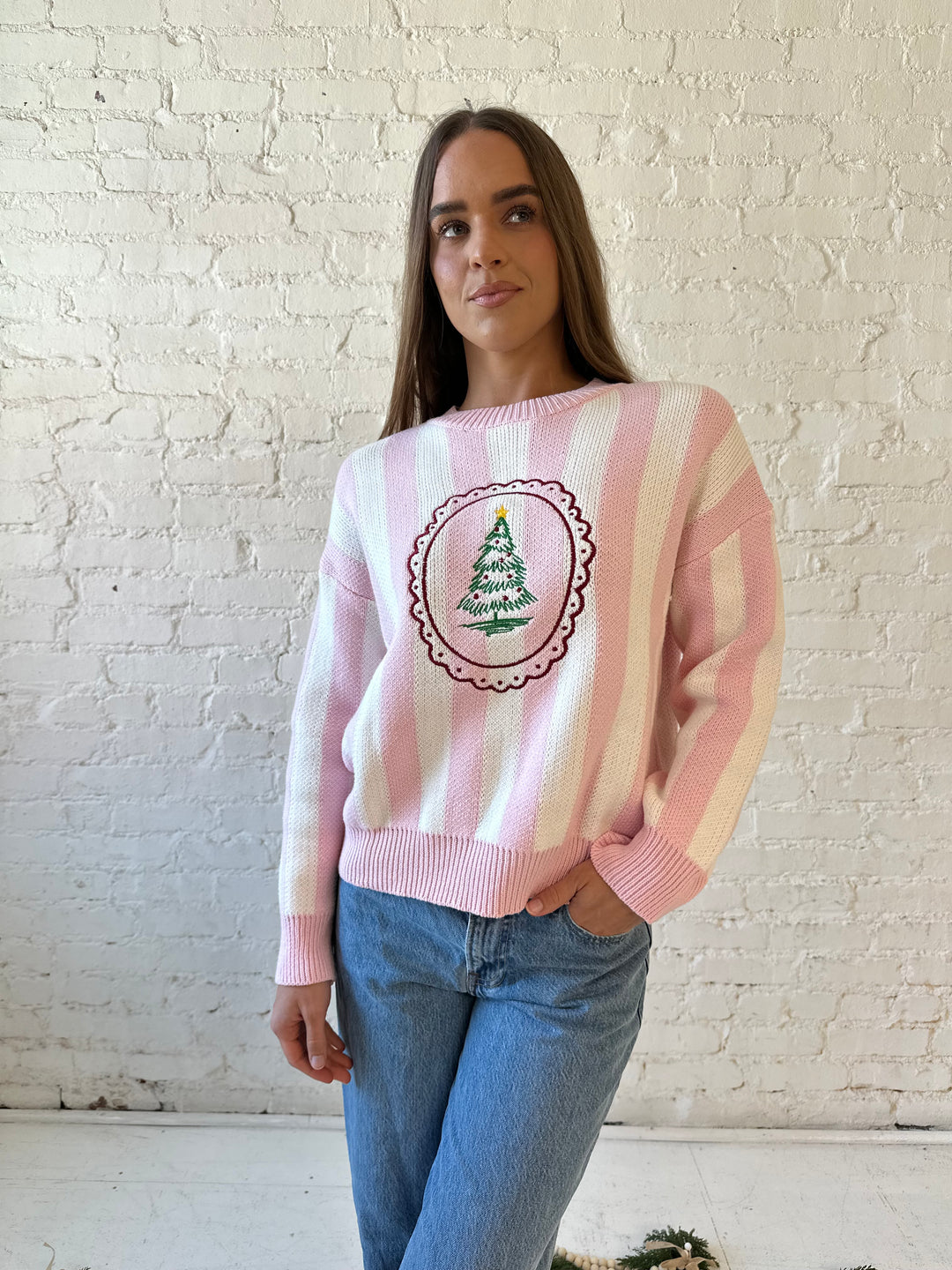 Woman wearing pink and white knit striped sweater with embroidered Christmas tree. 