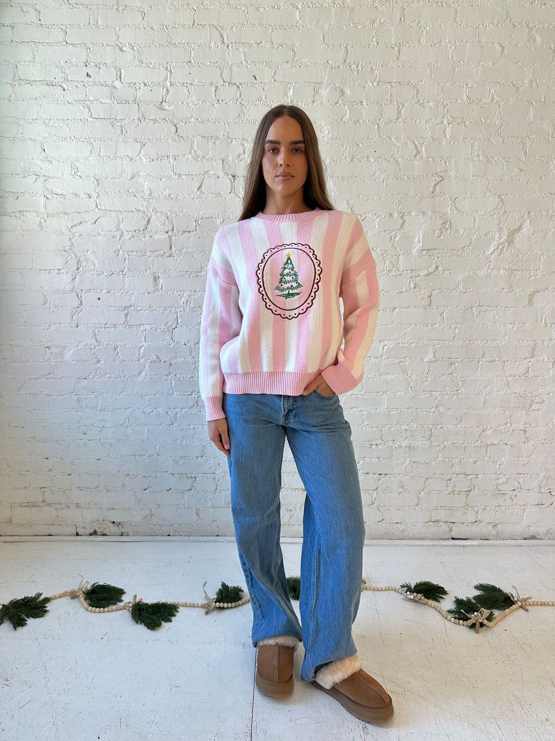 Woman wearing pink and white knit striped sweater with embroidered Christmas tree. 