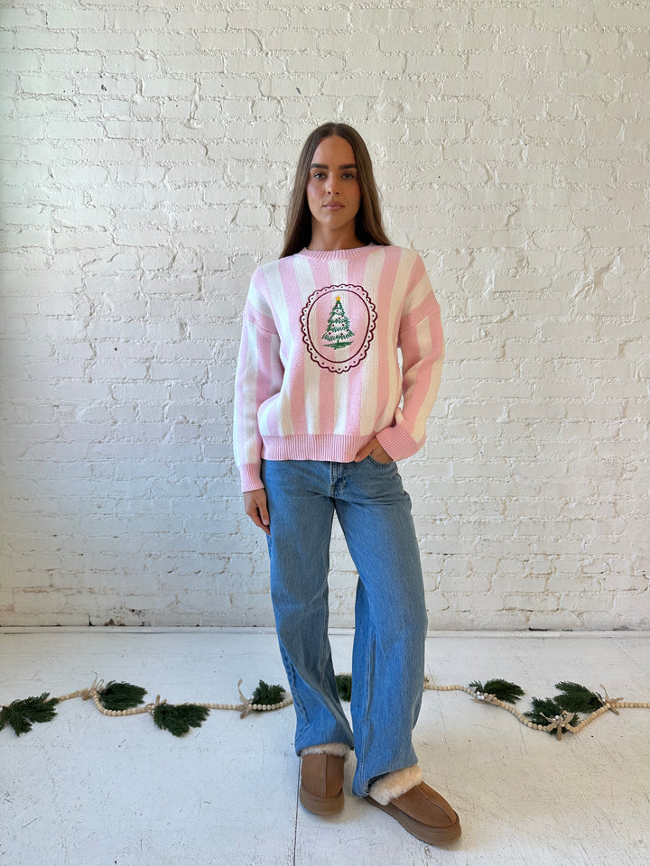 Woman wearing pink and white knit striped sweater with embroidered Christmas tree. 