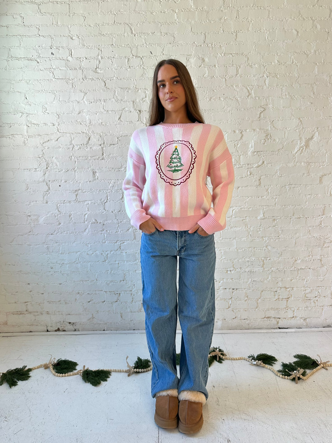 Woman wearing pink and white knit striped sweater with embroidered Christmas tree. 