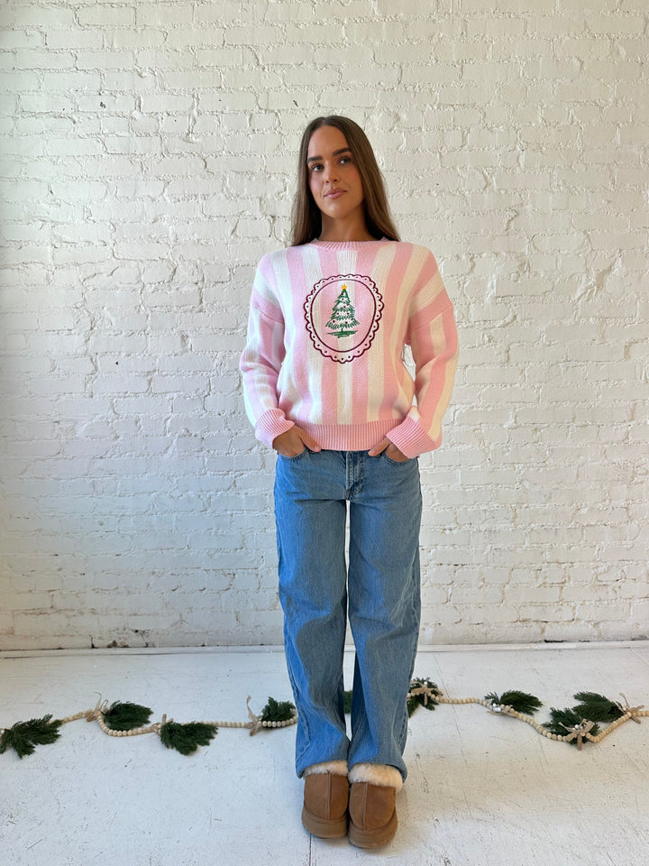 Woman wearing pink and white knit striped sweater with embroidered Christmas tree. 
