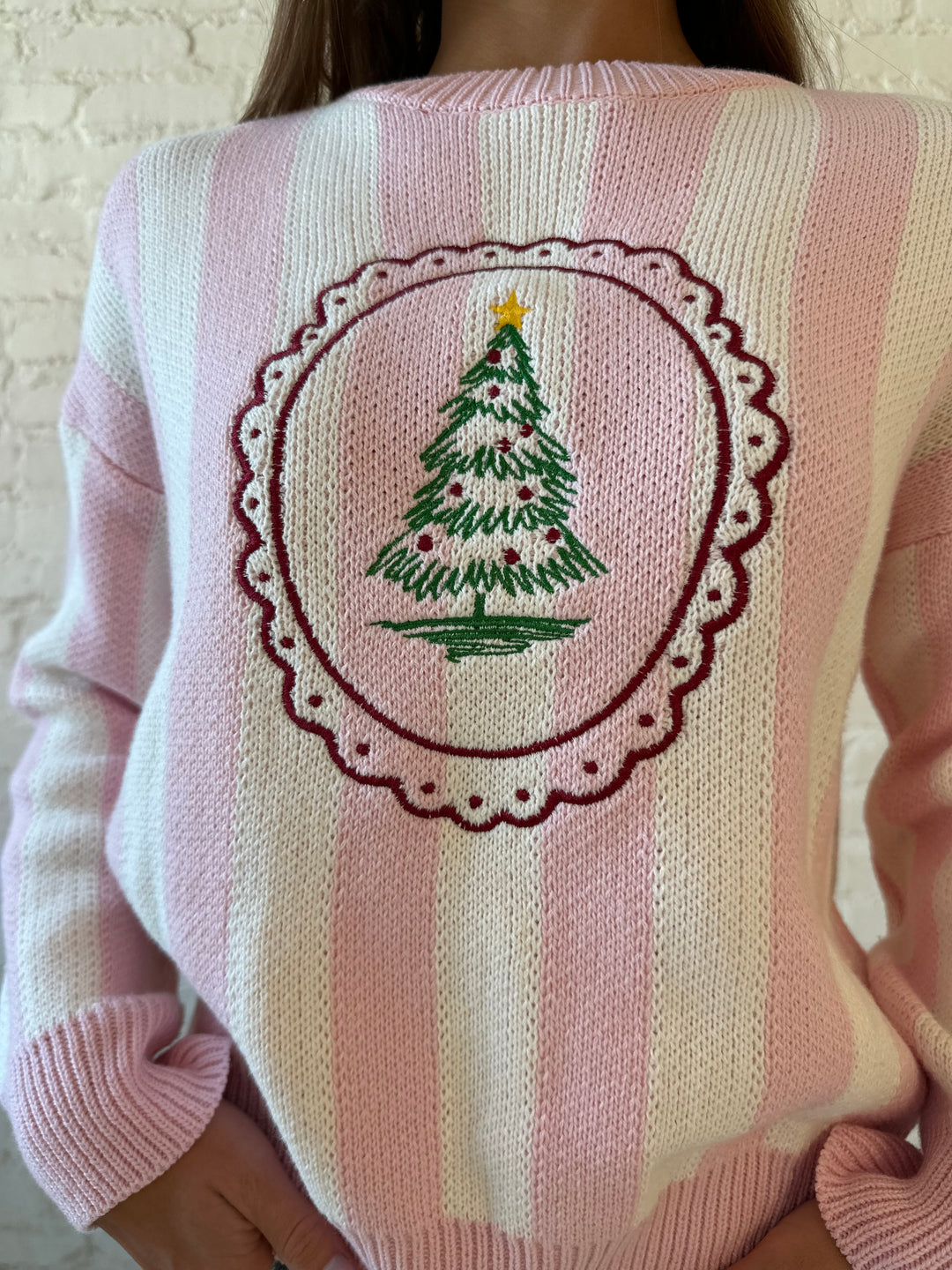 Woman wearing pink and white knit striped sweater with embroidered Christmas tree. 