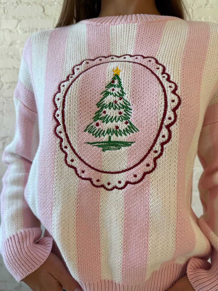 Woman wearing pink and white knit striped sweater with embroidered Christmas tree. 