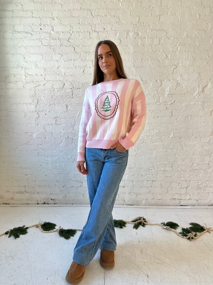 Woman wearing pink and white knit striped sweater with embroidered Christmas tree. 