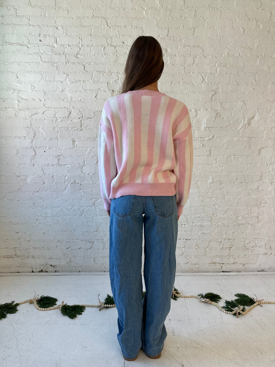 Woman wearing pink and white knit striped sweater with embroidered Christmas tree. 