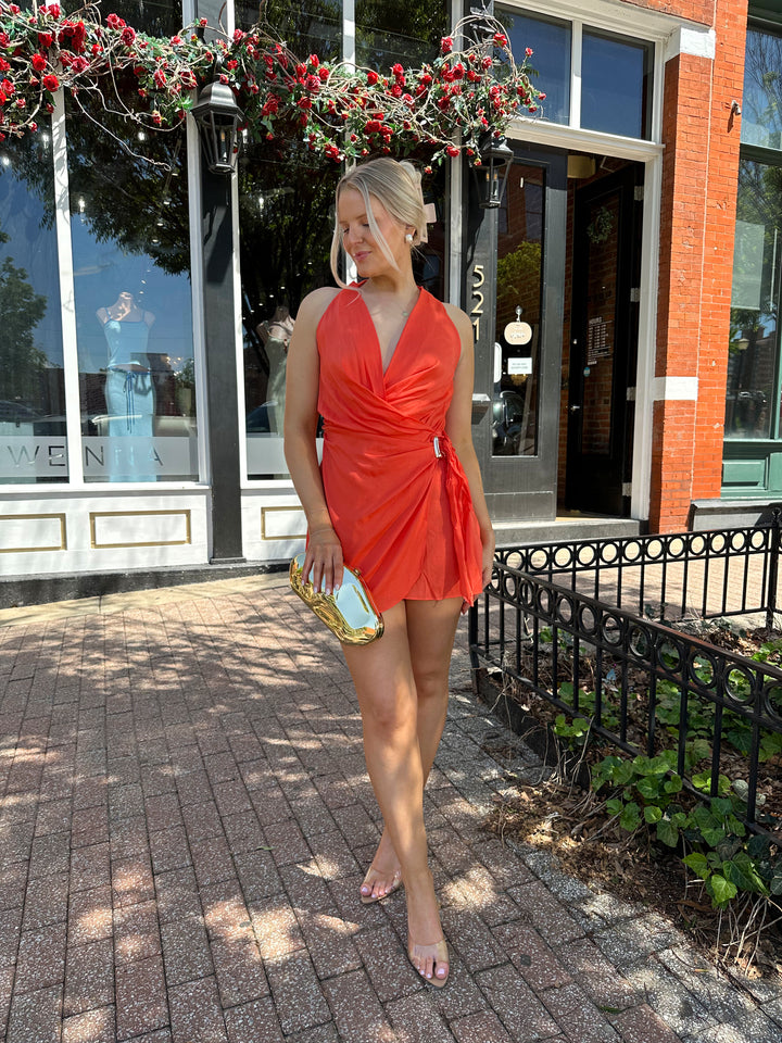 Woman wearing light weight color wrap mini dress with self tie halter neck, and gold hardware.