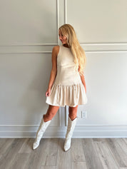 Woman wearing light beige drop waist mini dress with bow detail and cream knee boot.