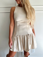 Woman wearing light beige drop waist mini dress with bow detail and cream knee boot.