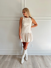 Woman wearing light beige drop waist mini dress with bow detail and cream knee boot.