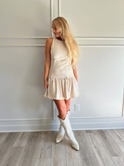 Woman wearing light beige drop waist mini dress with bow detail and cream knee boot.