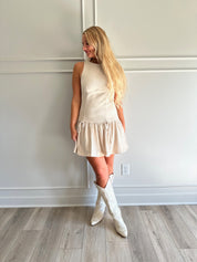 Woman wearing light beige drop waist mini dress with bow detail and cream knee boot.