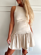 Woman wearing light beige drop waist mini dress with bow detail and cream knee boot.
