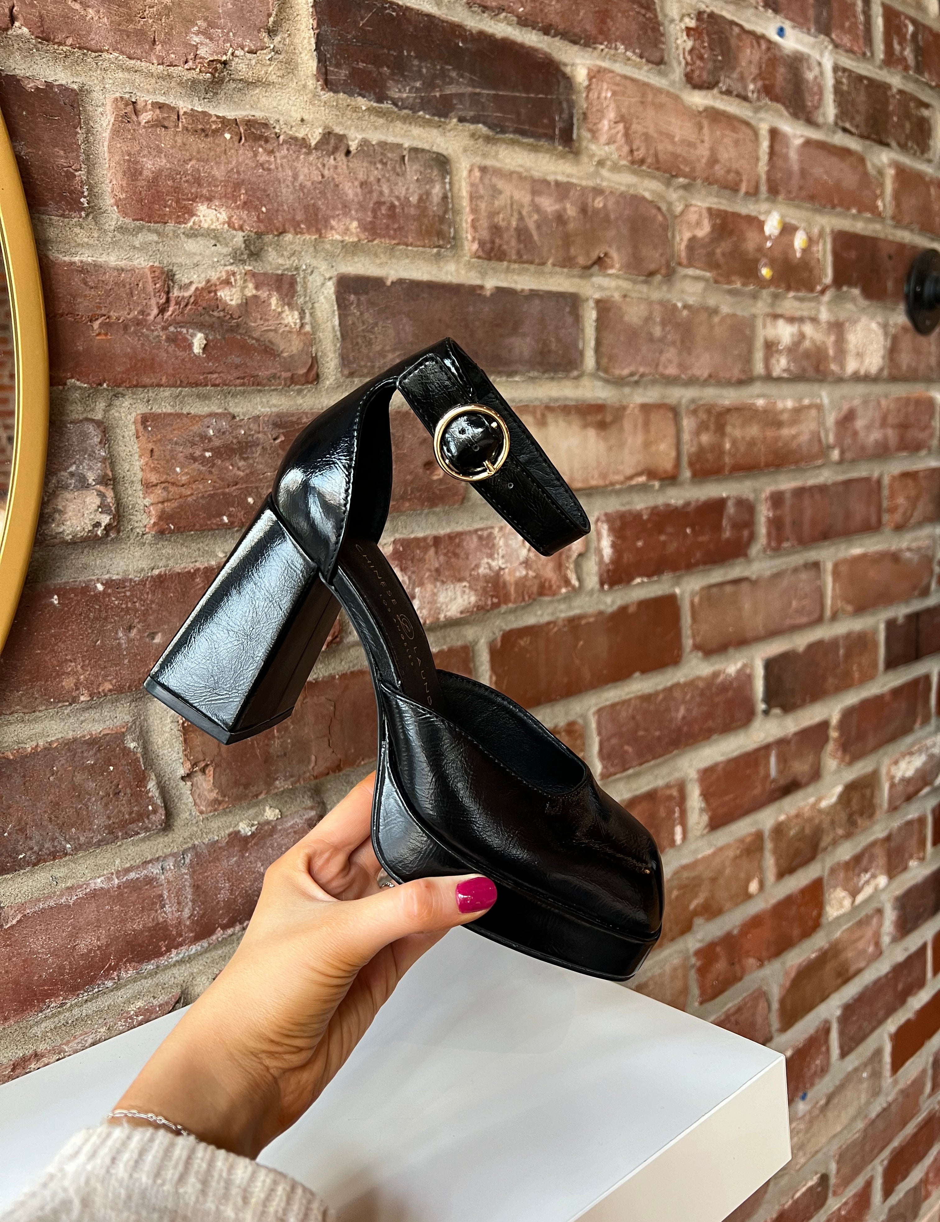 Black patent platform heel with closed toed front and ankle strap.