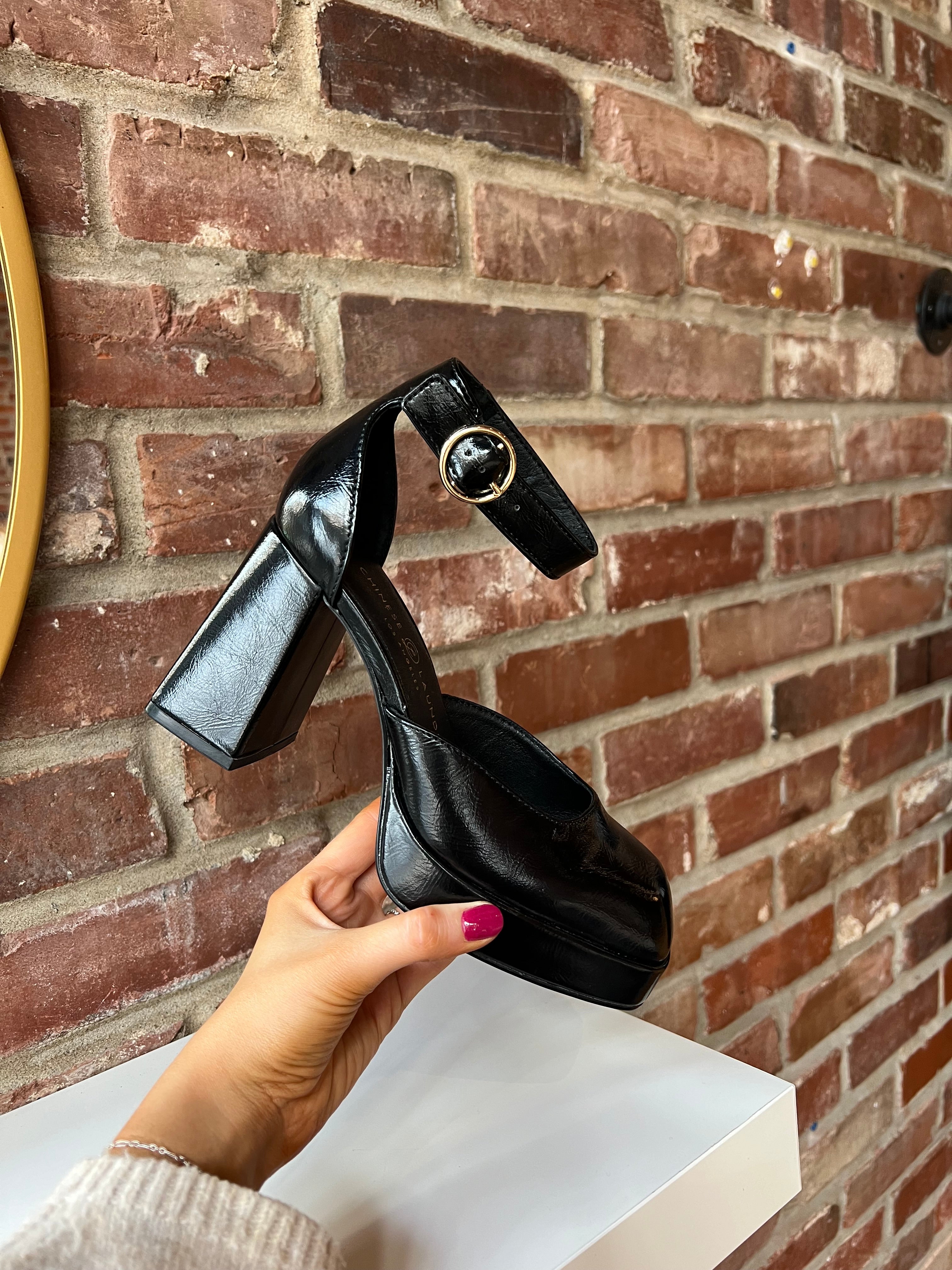 Black patent platform heel with closed toed front and ankle strap.