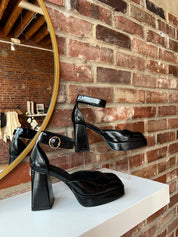 Black patent platform heel with closed toed front and ankle strap.