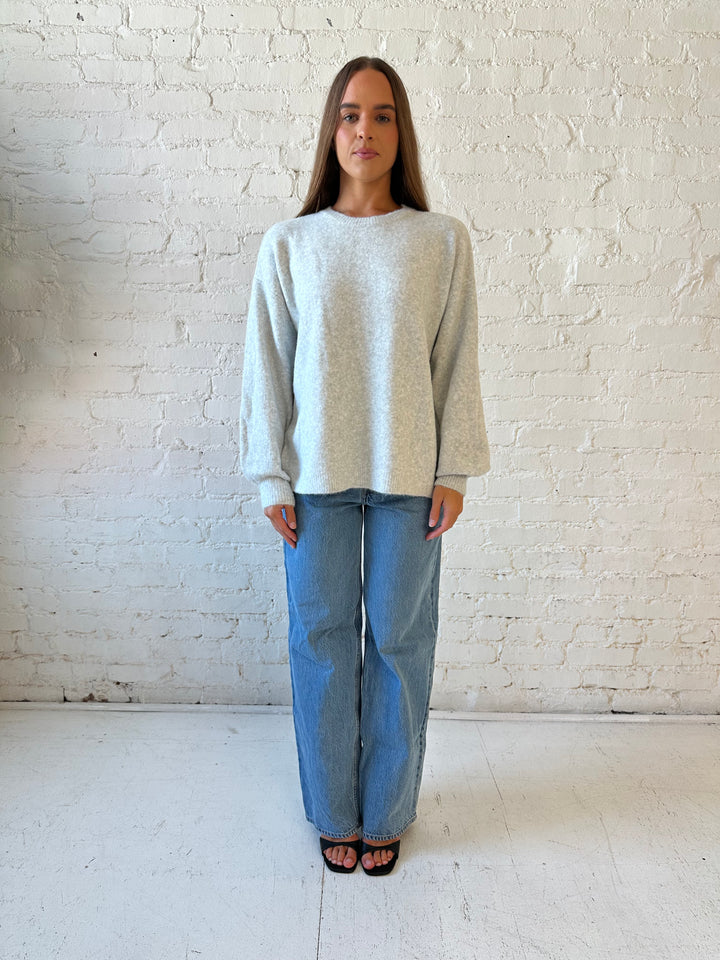 Woman wearing grey knit sweater with cream bow back detail with medium wash jeans. 