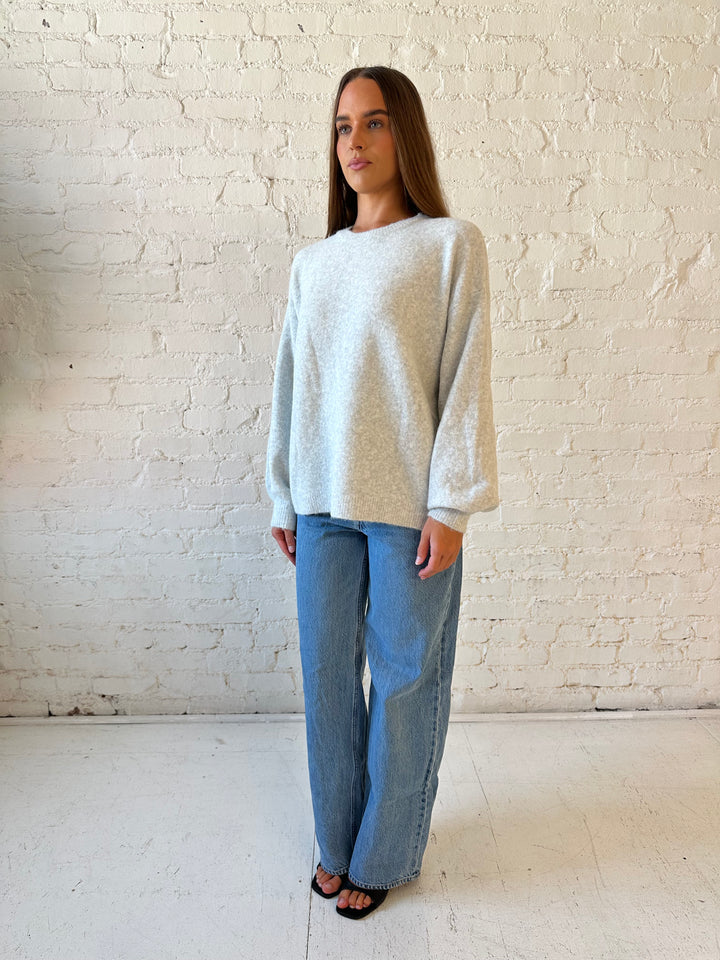 Woman wearing grey knit sweater with cream bow back detail with medium wash jeans. 