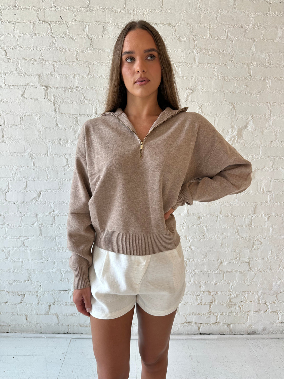 Woman wearing tan knit quarter zip sweater with cream shorts.