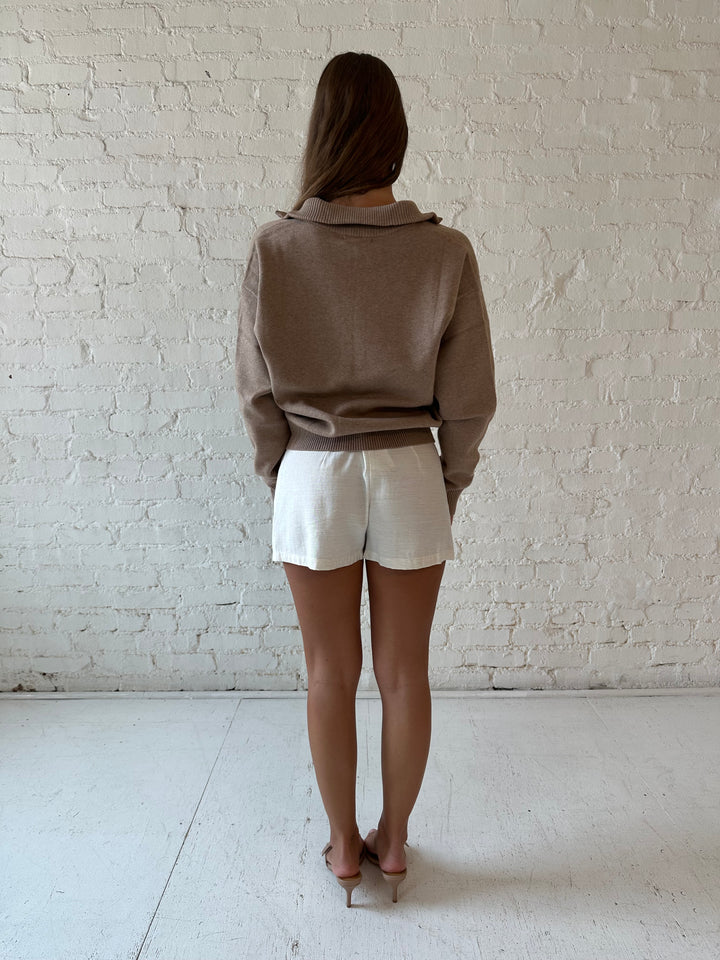 Woman wearing tan knit quarter zip sweater with cream shorts.