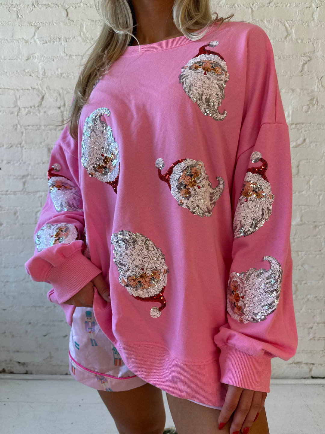 Woman wearing hot pink oversized pull over with multiple sequin santas all over. 