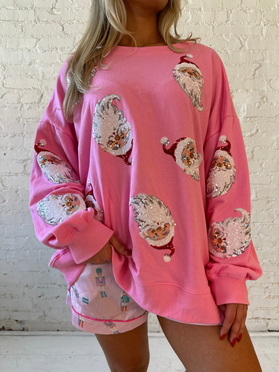 Woman wearing hot pink oversized pull over with multiple sequin santas all over. 