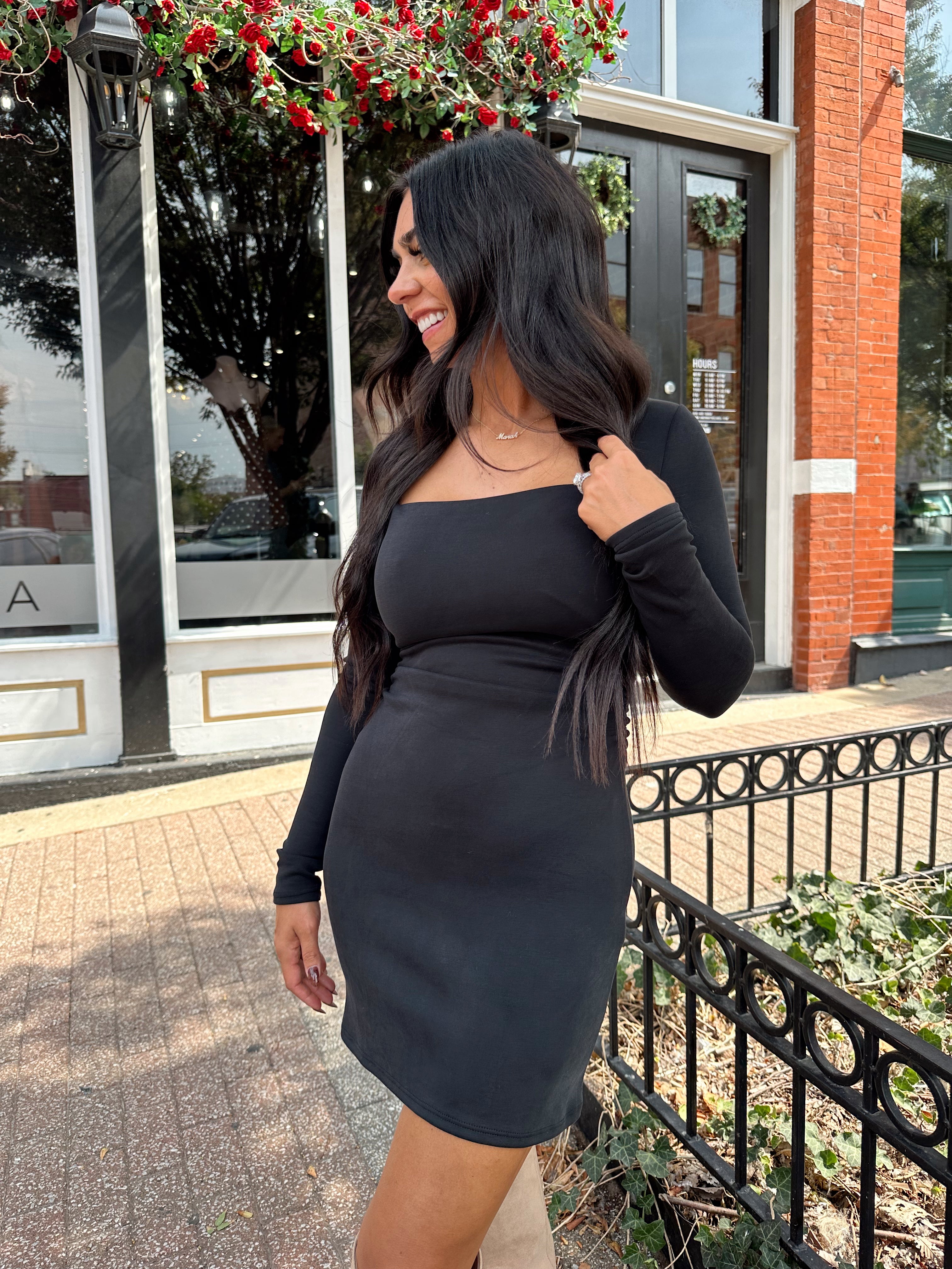 Woman wearing black long sleeve square neck mini dress with suede knee boot.