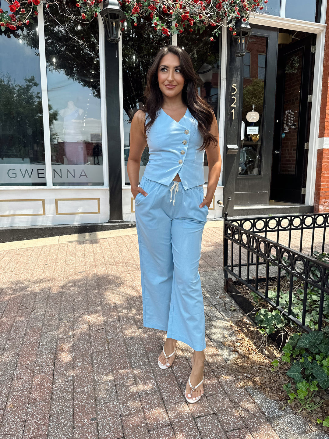Woman wearing light blue two piece set with vest top, and high waisted pant with draw string waist.