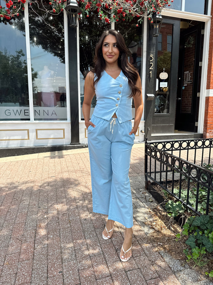 Woman wearing light blue two piece set with vest top, and high waisted pant with draw string waist.