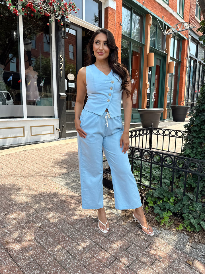 Woman wearing light blue two piece set with vest top, and high waisted pant with draw string waist.
