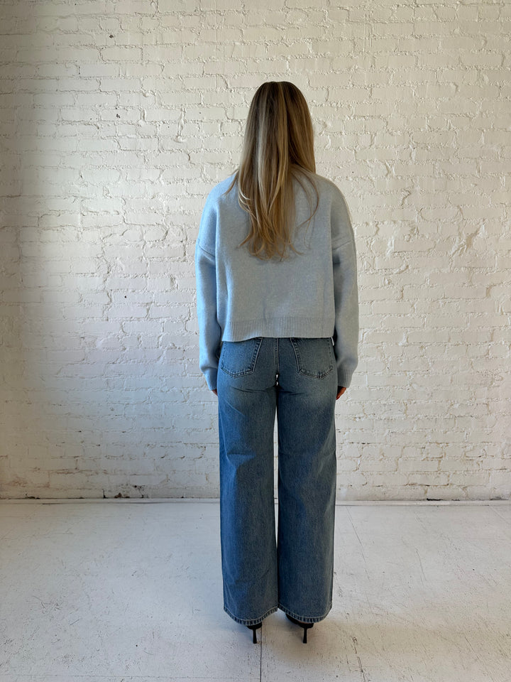 Woman wearing baby blue knit button down cardigan with medium wash wide leg jean. 