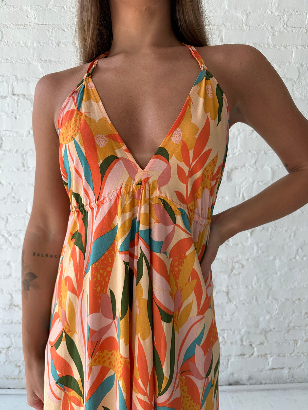 Woman wearing orange tropical print maxi dress with open back and tie detail.