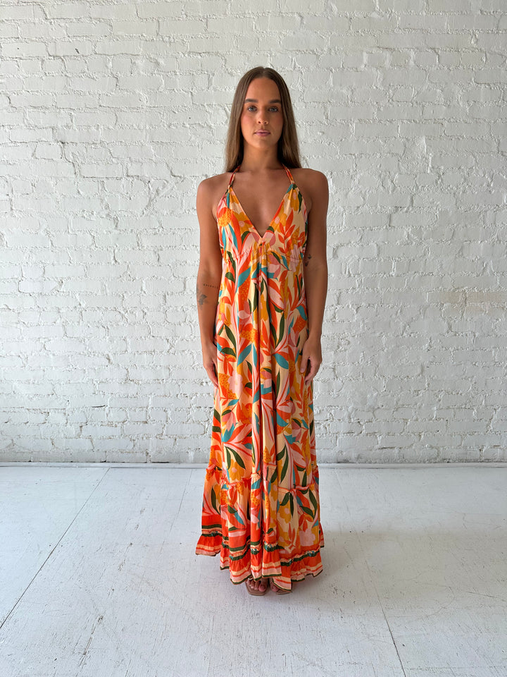 Woman wearing orange tropical print maxi dress with open back and tie detail.