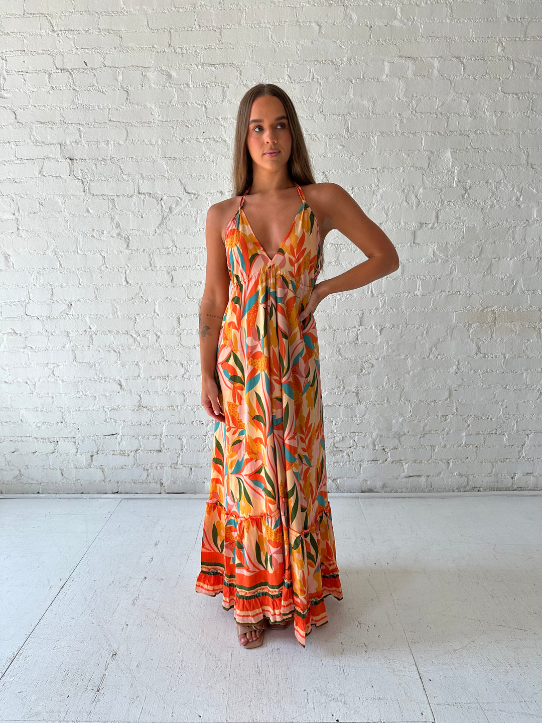 Woman wearing orange tropical print maxi dress with open back and tie detail.