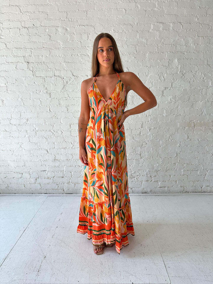 Woman wearing orange tropical print maxi dress with open back and tie detail.