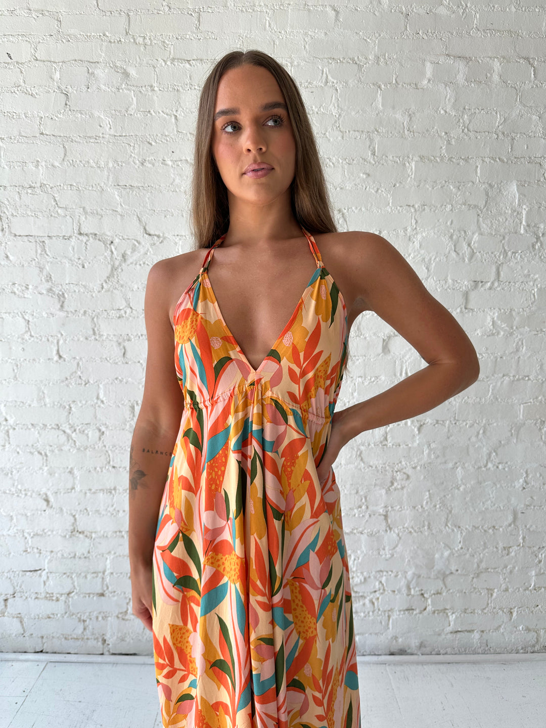 Woman wearing orange tropical print maxi dress with open back and tie detail.