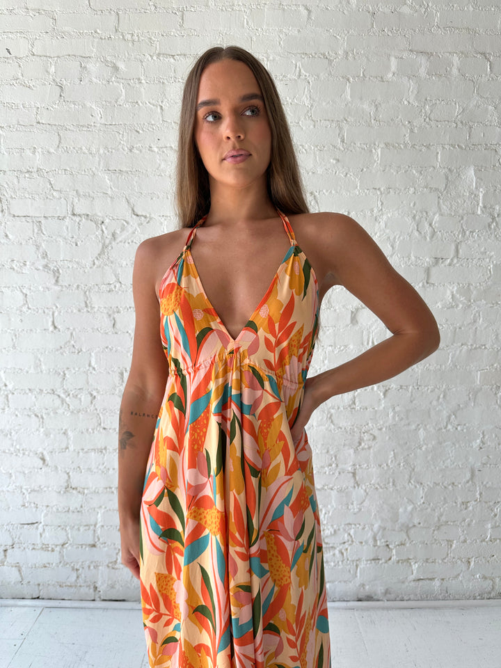 Woman wearing orange tropical print maxi dress with open back and tie detail.