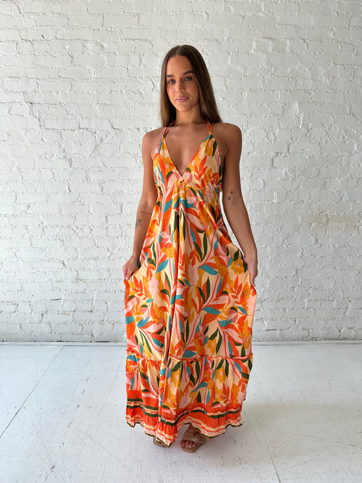 Woman wearing orange tropical print maxi dress with open back and tie detail.