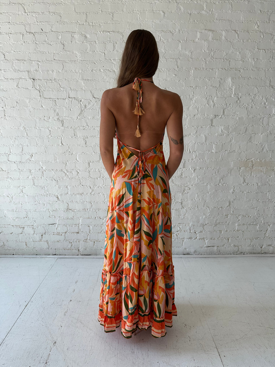 Woman wearing orange tropical print maxi dress with open back and tie detail.
