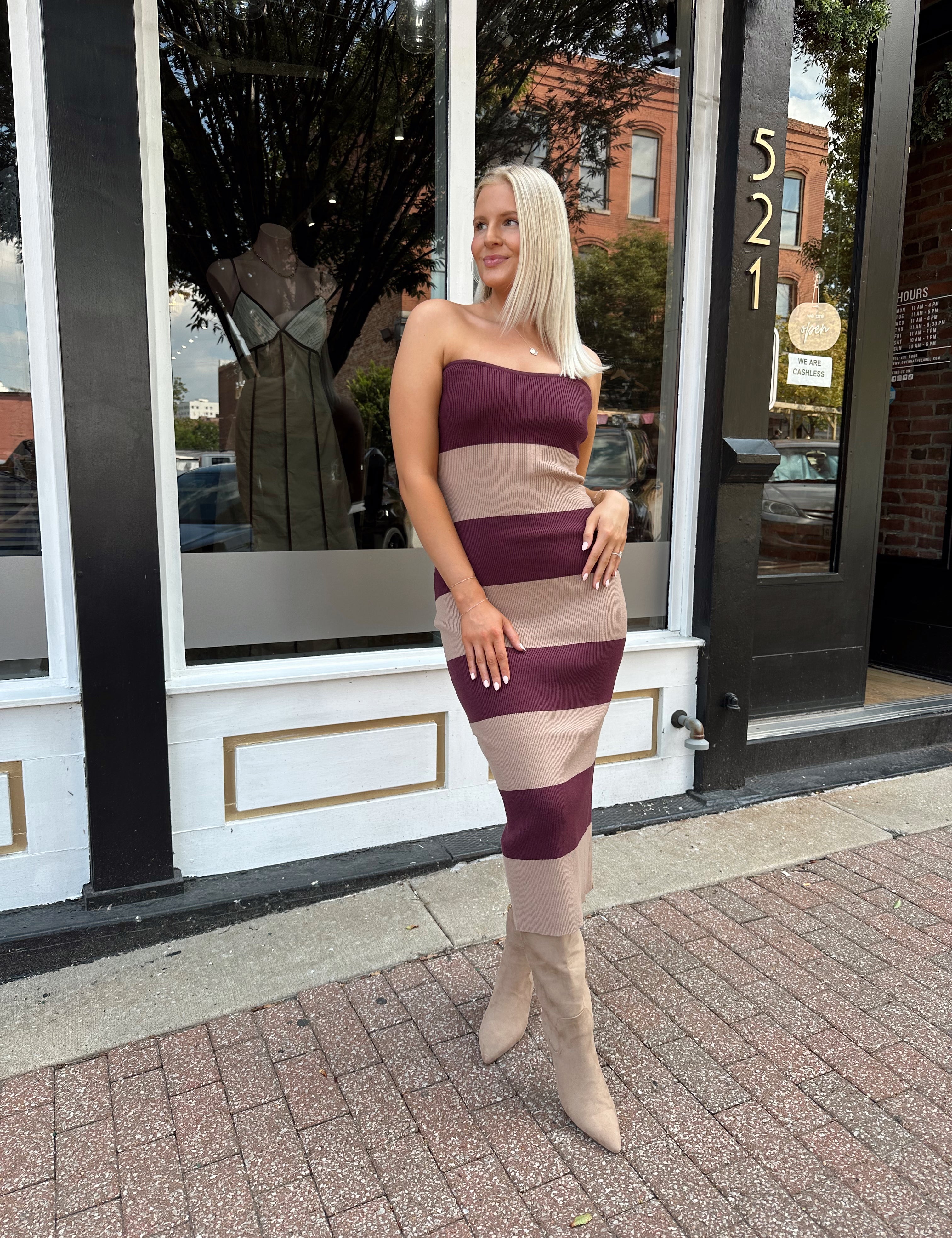 Woman wearing strapless maroon and beige striped knit midi dress with knee-high beige boots.