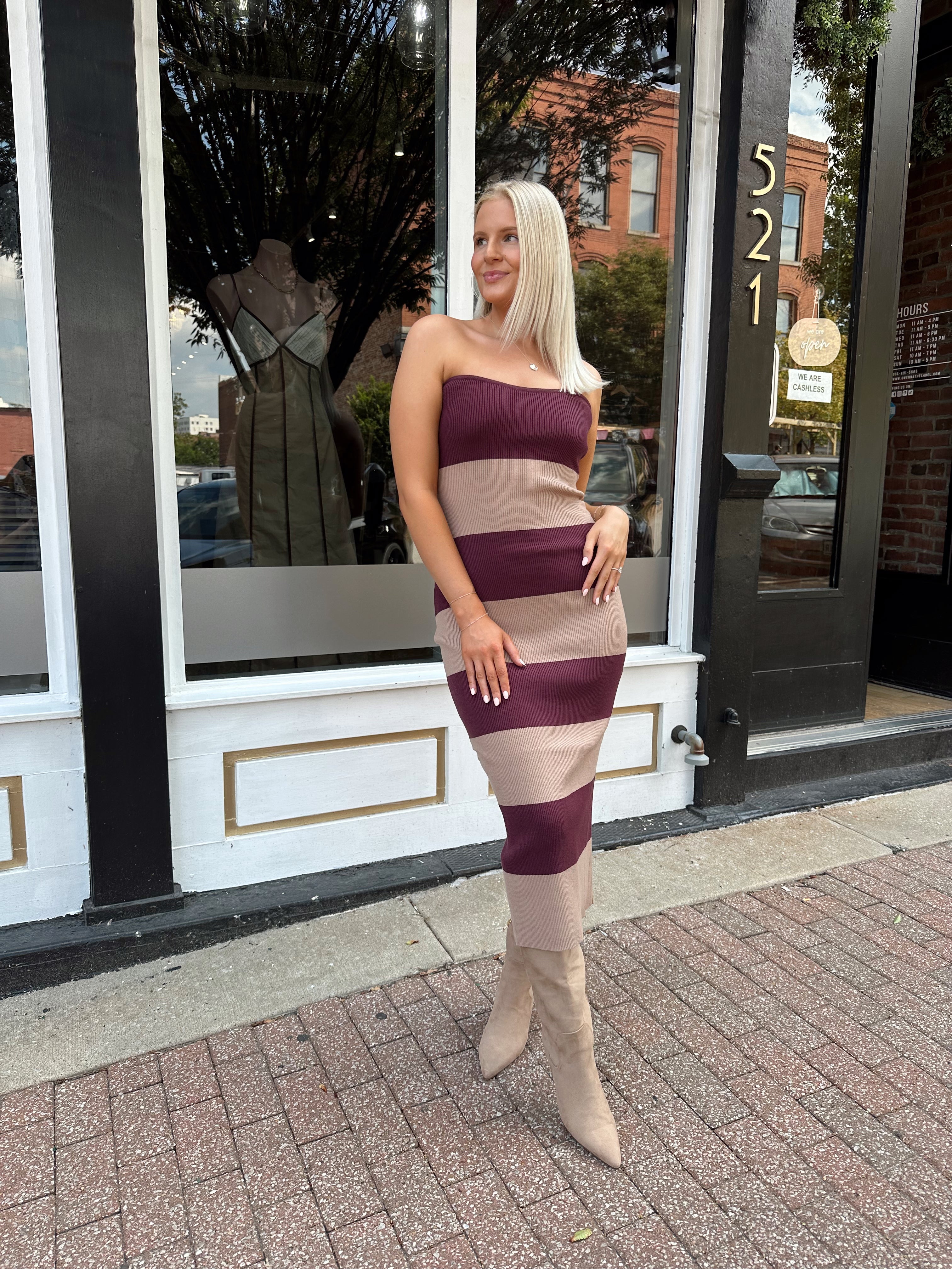 Woman wearing strapless maroon and beige striped knit midi dress with knee-high beige boots.
