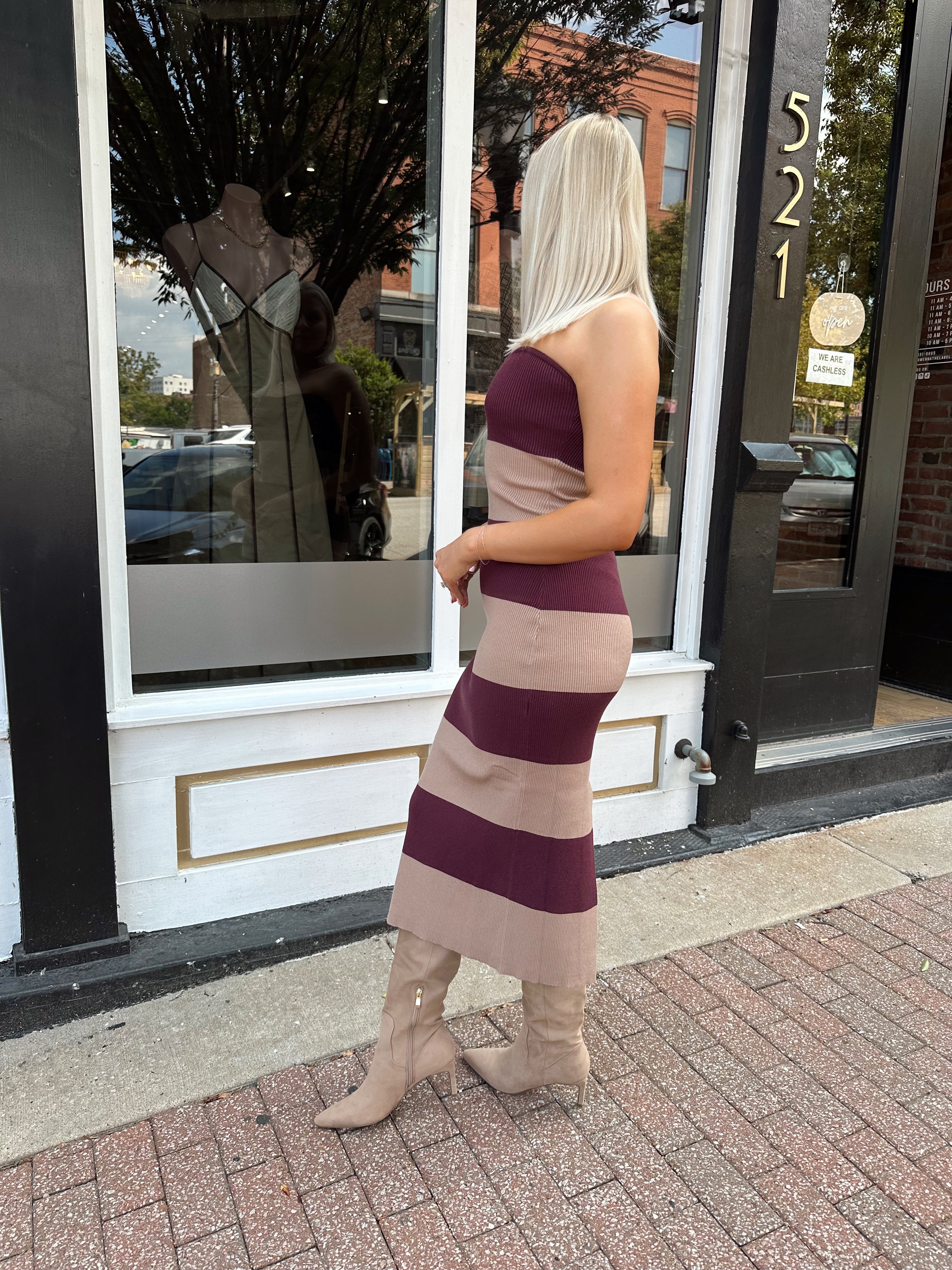 Woman wearing strapless maroon and beige striped knit midi dress with knee-high beige boots.