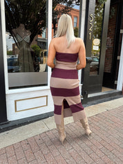 Woman wearing strapless maroon and beige striped knit midi dress with knee-high beige boots.