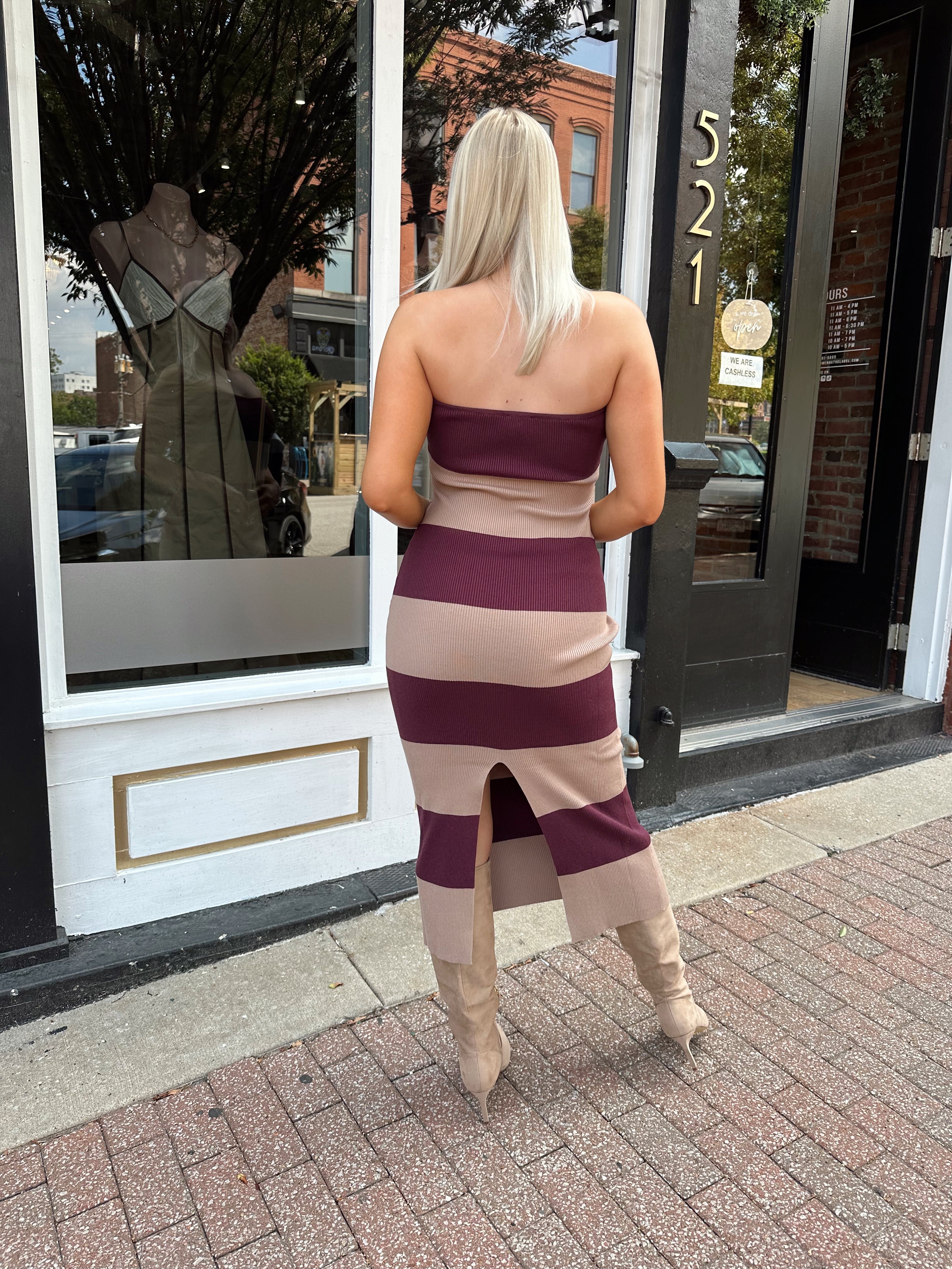 Woman wearing strapless maroon and beige striped knit midi dress with knee-high beige boots.