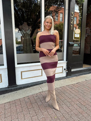 Woman wearing strapless maroon and beige striped knit midi dress with knee-high beige boots.