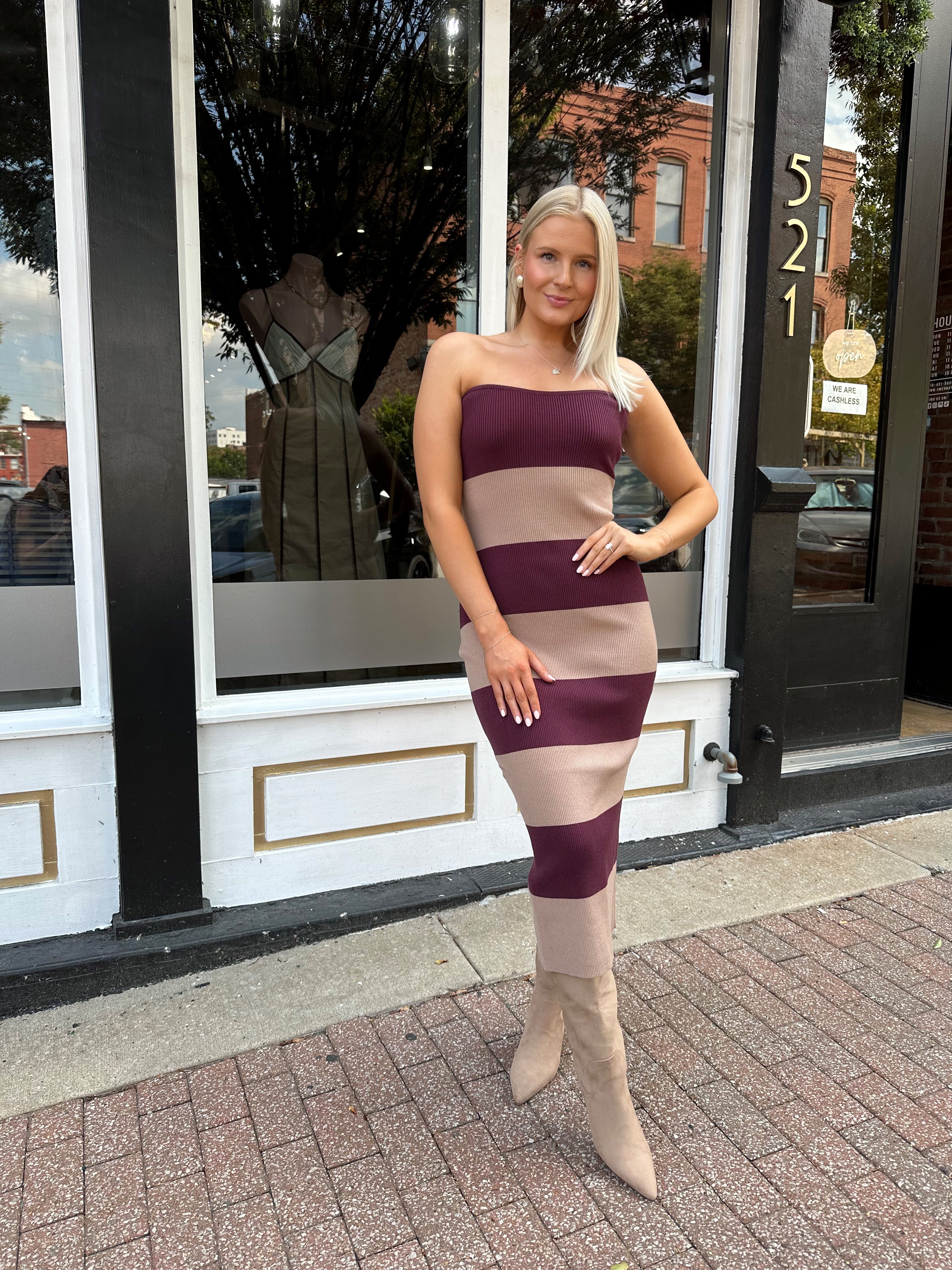 Woman wearing strapless maroon and beige striped knit midi dress with knee-high beige boots.