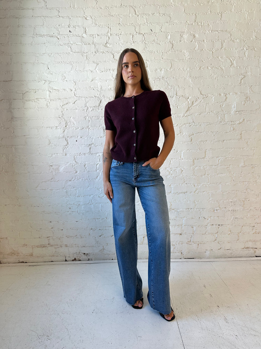 Woman wearing medium wash wide leg jeans with a raw hem, and burgundy sweater top. 